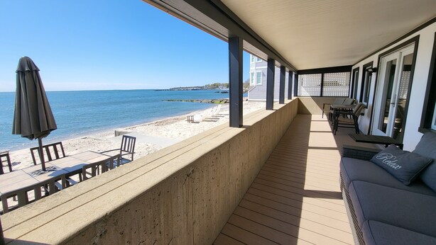 Ein überdachter Außenbereich mit Blick auf den Strand, einer Holzterrasse und Sitzgelegenheiten.