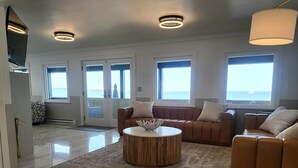 Ein geräumiger Wohnbereich mit einer braunen Ledersofa, einem runden Couchtisch und großen Fenstern mit Meerblick.