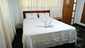 A neatly made bed with white linens and a towel, a wooden nightstand, and a wooden door with a sign. - Puerto Azul  (Sauce)