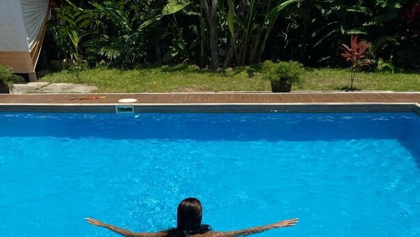 A poolside area with a person swimming, a towel, sunglasses, a drink, and a bottle of sunscreen. - Puerto Azul  (Sauce)