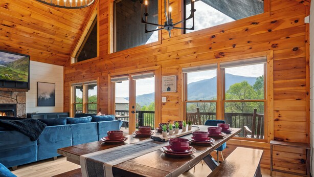 A wooden cabin with a dining table set for four, a blue sofa, and a fireplace.