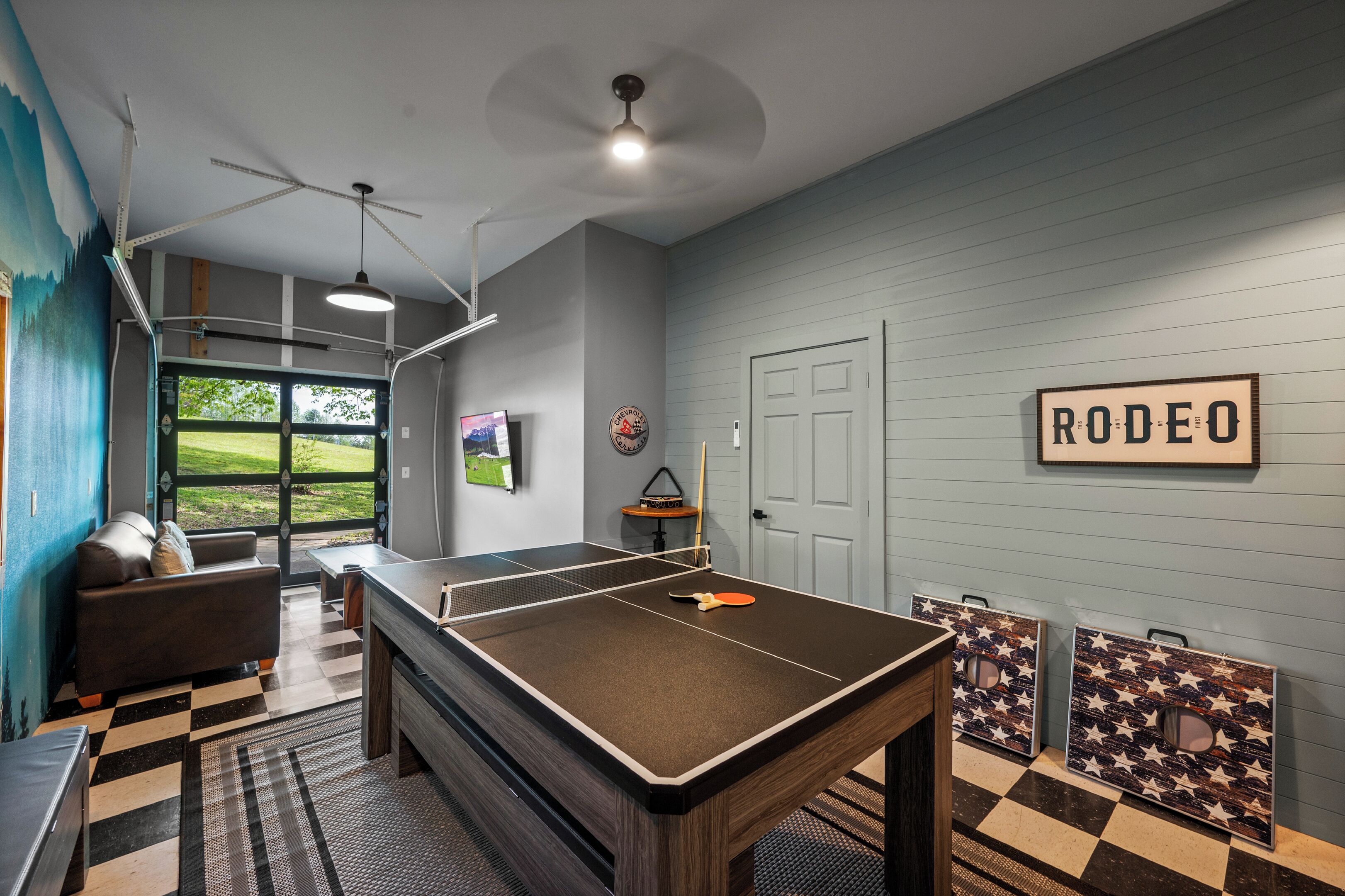 Een kamer met een pingpongtafel, een bank, een plafondventilator en een deur met de tekst 'RODEO'.