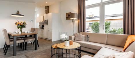 Uma sala de estar moderna com sofá, mesa de centro, mesa de jantar e cadeiras. Janelas amplas oferecem vista para o exterior.