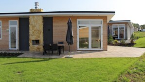 Ein modernes Haus mit Natursteinfassade, großen Glasfenstern und einer Terrasse mit Gartenmöbeln.