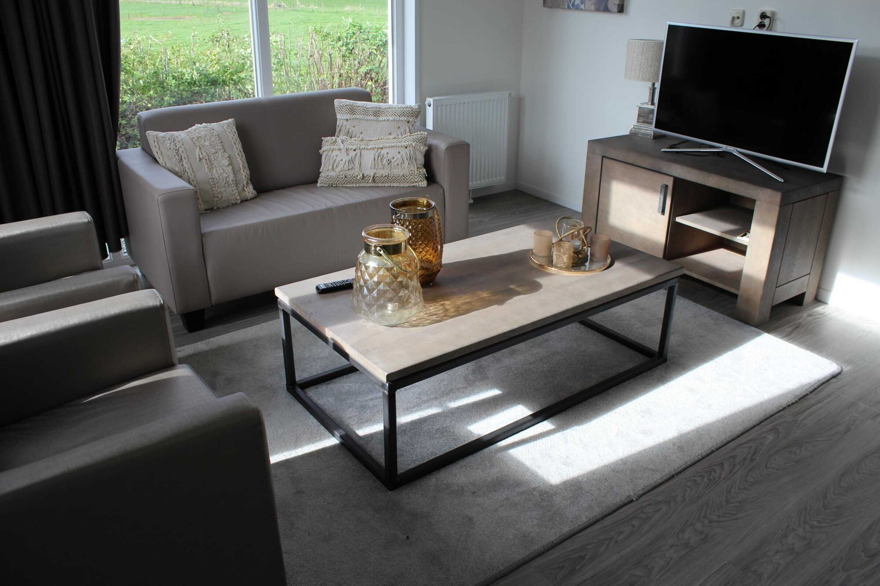 Ein modernes Wohnzimmer mit einer Couch, einem Couchtisch, einer TV-Konsole und Blick ins Freie.
