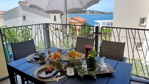 A balcony table with a table umbrella, a plate of food, and a view of the sea. - Vacation apartment Happy Olive in Sevid near Trogir Croatia (Sevid na moru)