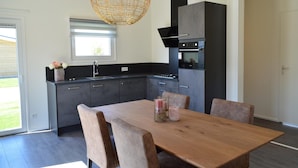 A modern kitchen with dark cabinetry, a wooden dining table, and a large pendant light. - Holiday Home in Bemelen Near Nature Reserve (Bemelen)
