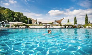 Une piscine entourée de verdure, avec des chaises longues et des parasols, sous un ciel dégagé.