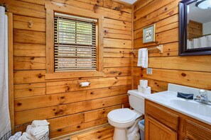 A wooden cabin bathroom with a toilet, sink, and window with blinds. - Slopeside | Hocking Hills Retreat, Covered Hot Tub (Laurelville)