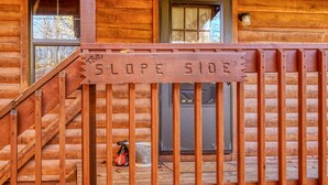 A wooden cabin with a sign reading "SLOPE SIDE" and a staircase leading to a door. - Slopeside | Hocking Hills Retreat, Covered Hot Tub (Laurelville)