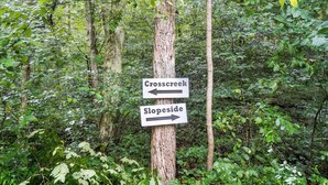 Ein Wegweiser in einem bewaldeten Gebiet zeigt mit zwei Pfeilen nach links und rechts, beschriftet mit 'Crosscreek' und 'Slopeside'.