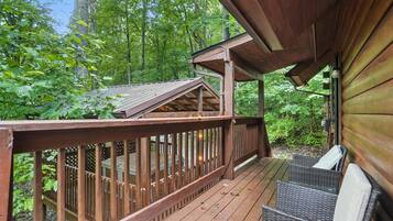A wooden deck with wicker furniture, surrounded by dense forest.