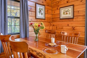 A wooden dining table with chairs, a vase with flowers, and framed botanical prints on the wall.