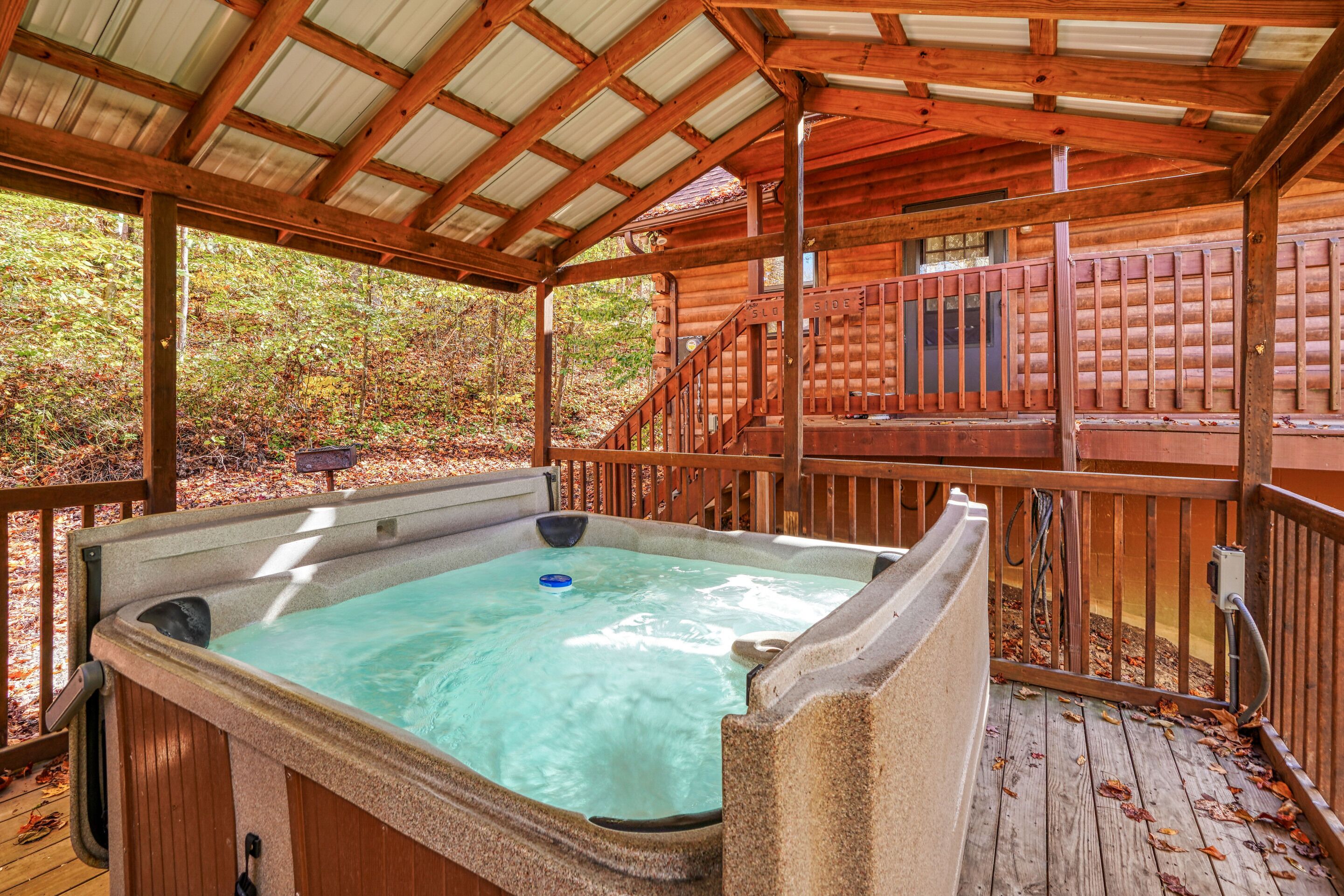 A hot tub under a wooden deck with a view of a cabin in the background.