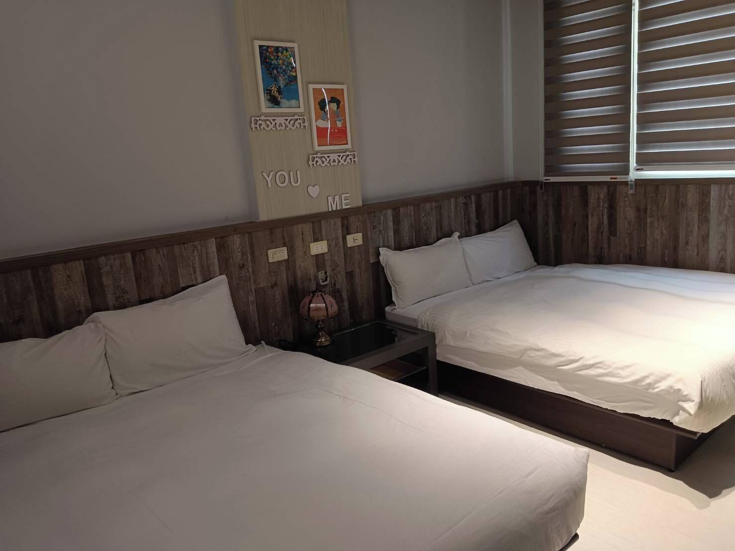 A bedroom with two beds, wooden headboards, a wall decoration, and a window with blinds.