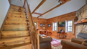 A wooden staircase leading to a living area with a stone fireplace, wooden walls, and a dining table. - Crosscreek | Hocking Hills, 6 Acres, Hot Tub, Pets (Laurelville)