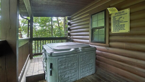A log cabin with a hot tub on the porch, a sign with spa rules, and a view of the forest. - Crosscreek | Hocking Hills, 6 Acres, Hot Tub, Pets (Laurelville)