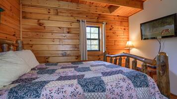 Una habitación de cabaña de madera con una cama, una ventana con cortinas, una lámpara y un cuadro en la pared.