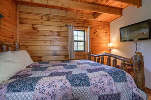 Une pièce de style cabane en bois, avec un lit, une fenêtre avec des rideaux, une lampe et un tableau accroché au mur.