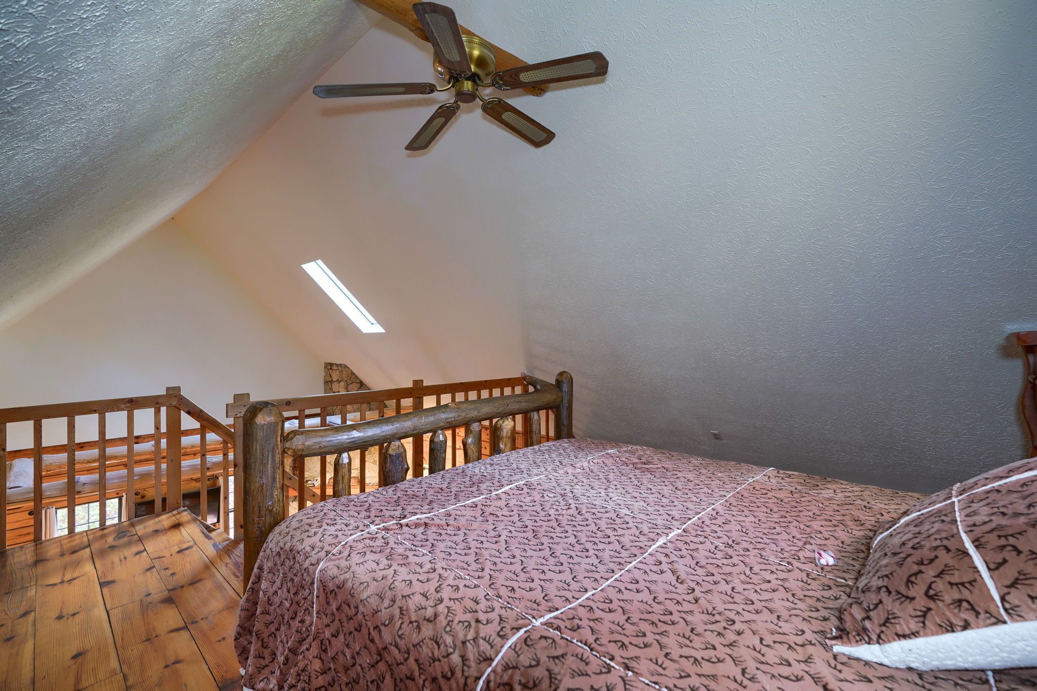 Ein Schlafzimmer mit einem hölzernen Bettgestell, einer gemusterten Bettdecke, einem Deckenventilator und einem Holzlaufgeländer.