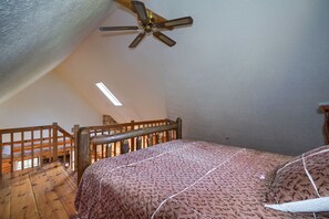 Une chambre à coucher avec un cadre de lit en bois, une couvre-lit à motifs, un ventilateur de plafond et une balustrade en bois.