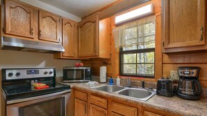 Una cocina con armarios de madera, electrodomésticos de acero inoxidable, un lavamanos doble y un ventanal con vistas a árboles.