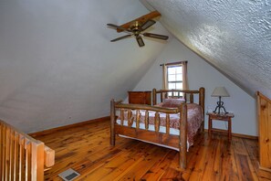 A bedroom with a sloped ceiling, a wooden bed, a nightstand, a lamp, and a window.