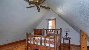 Un dormitorio con una cama de madera, un ventilador de techo, una mesita de noche, una lámpara y una ventana con cortinas.