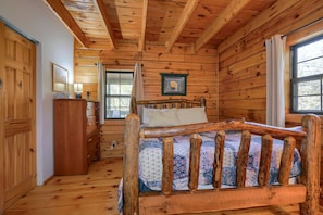 Une chambre à coucher dans une cabane en bois, avec un lit, une commode et deux fenêtres.