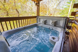 A hot tub with a wooden deck and a view of autumn trees.