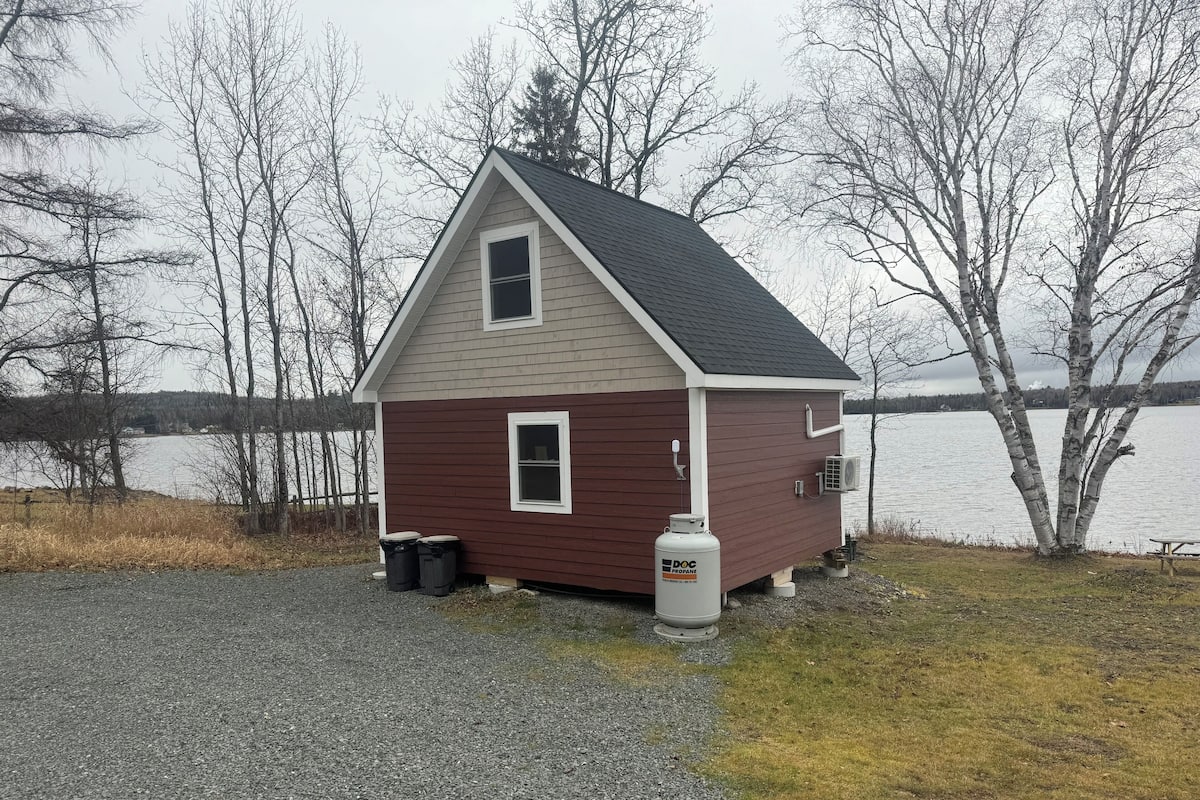 A small, single-story cabin with a gabled roof, positioned near a body of water.