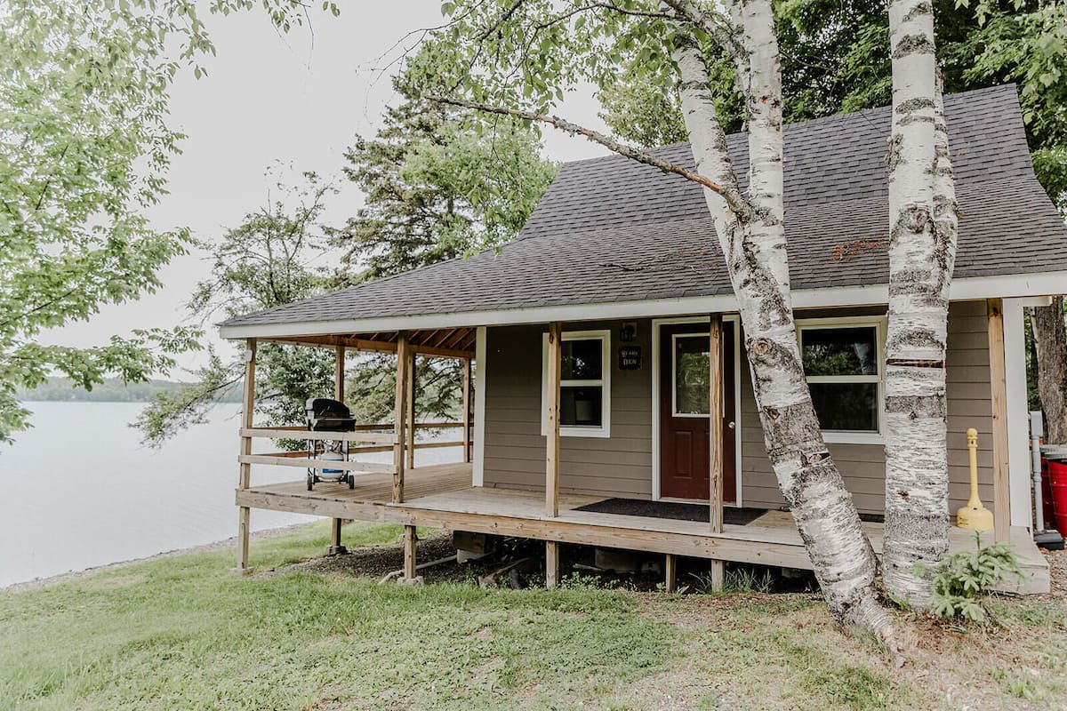 A cabin with a wooden deck, a covered porch, and a view of a lake.