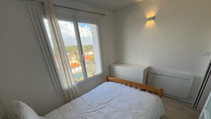 Ett sovrum med en stor säng, ett fönster med gardiner, en vit byrå och ett element.