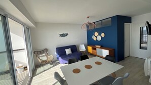 Ett modernt vardagsrum med en matplats, en soffa, ett soffbord och utsikt genom en skjutdörr.