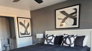 A modern bedroom with a large bed, a ceiling fan, and abstract artwork on the walls. - Rodeo-Ready Retreat! Newly Renovated & Stylishly Relaxing (Houston)