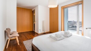 Moderni hotellihuone, jossa on suuri sänky, puinen vaatekaappi ja näkymä kaupunkiin.