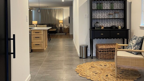 A modern living room with a black bookshelf, a wicker chair, and a dining area in the background. - Charming 4-bedroom house with WiFi and AC in enchanting Houston (Houston)