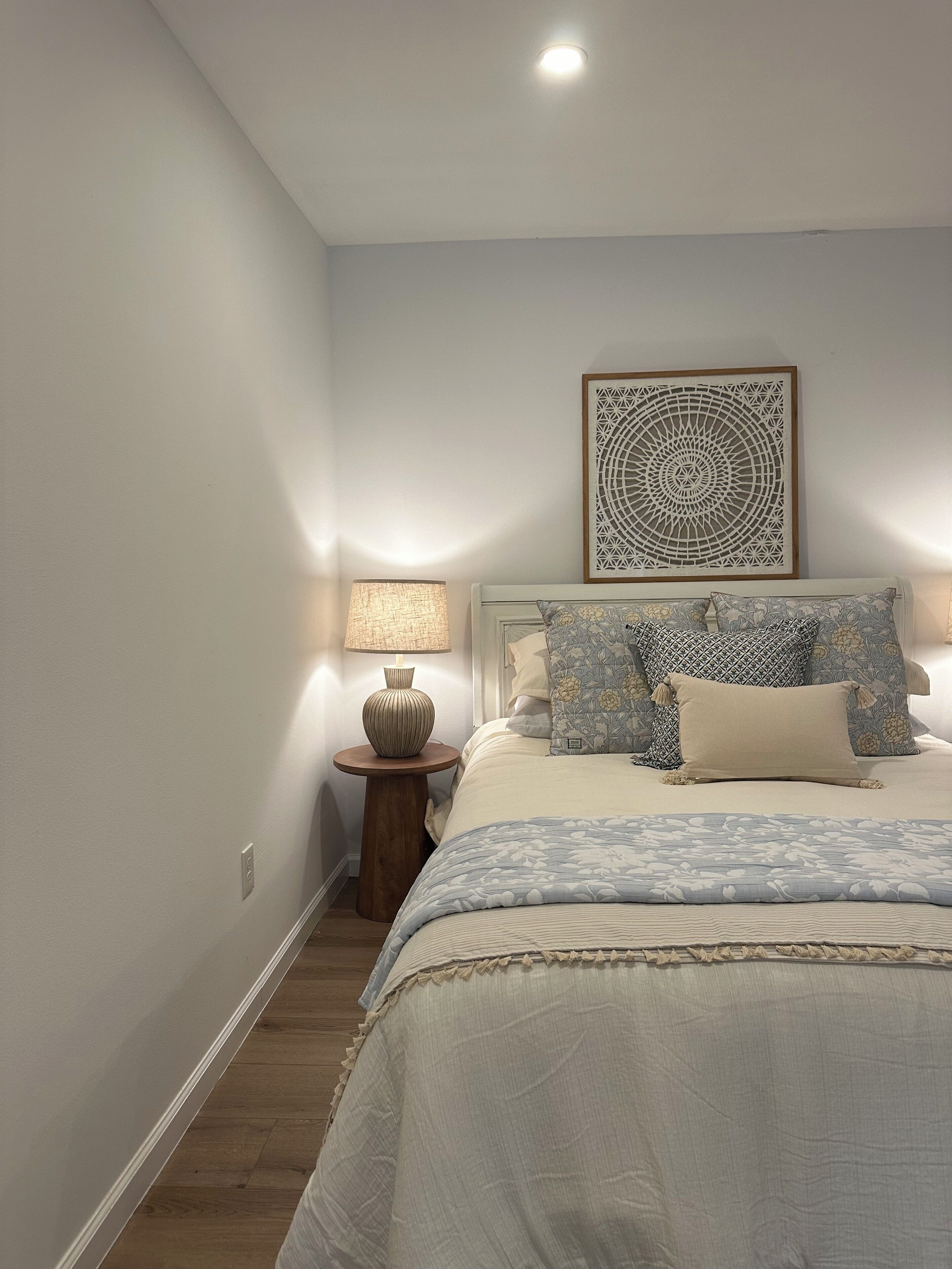 Une chambre à coucher avec un lit, une table de chevet, une lampe et un élément décoratif mural.