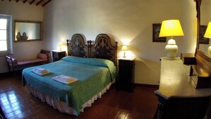 Une chambre avec un plafond en bois, un lit recouvert d’une couverture verte, deux lampes de chevet, une table de chevet, une chaise et une commode avec un miroir.