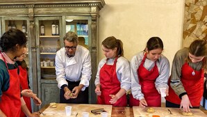 Un groupe de personnes se trouve dans une cuisine, porte des tabliers et prépare des aliments.