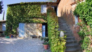 Un bâtiment rustique en pierre, avec une allée de gravier, un banc en bois et des plantes en pot.