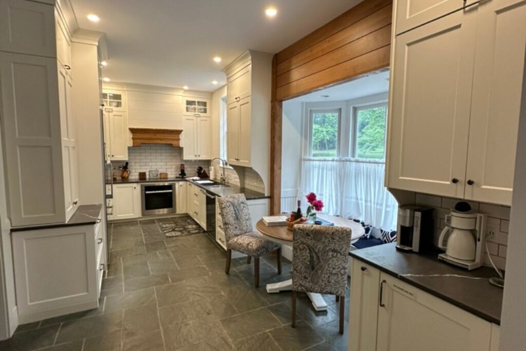 A modern kitchen with white cabinetry, a dining area with patterned chairs, and a coffee maker on the counter.