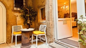 A rustic stone building with a small outdoor seating area featuring two white chairs with yellow cushions, a round stone table, and a hanging light fixture. - La Chaumière - BedinShop - historic center - France (Romans-sur-Isère)