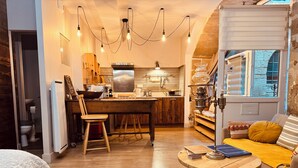 A cozy living room with a wooden dining table, a sofa with cushions, and a round coffee table. - La Chaumière - BedinShop - historic center - France (Romans-sur-Isère)