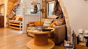 A cozy loft-style room with a wooden ceiling, a round wooden table, a sofa, and a window with curtains. - La Chaumière - BedinShop - historic center - France (Romans-sur-Isère)
