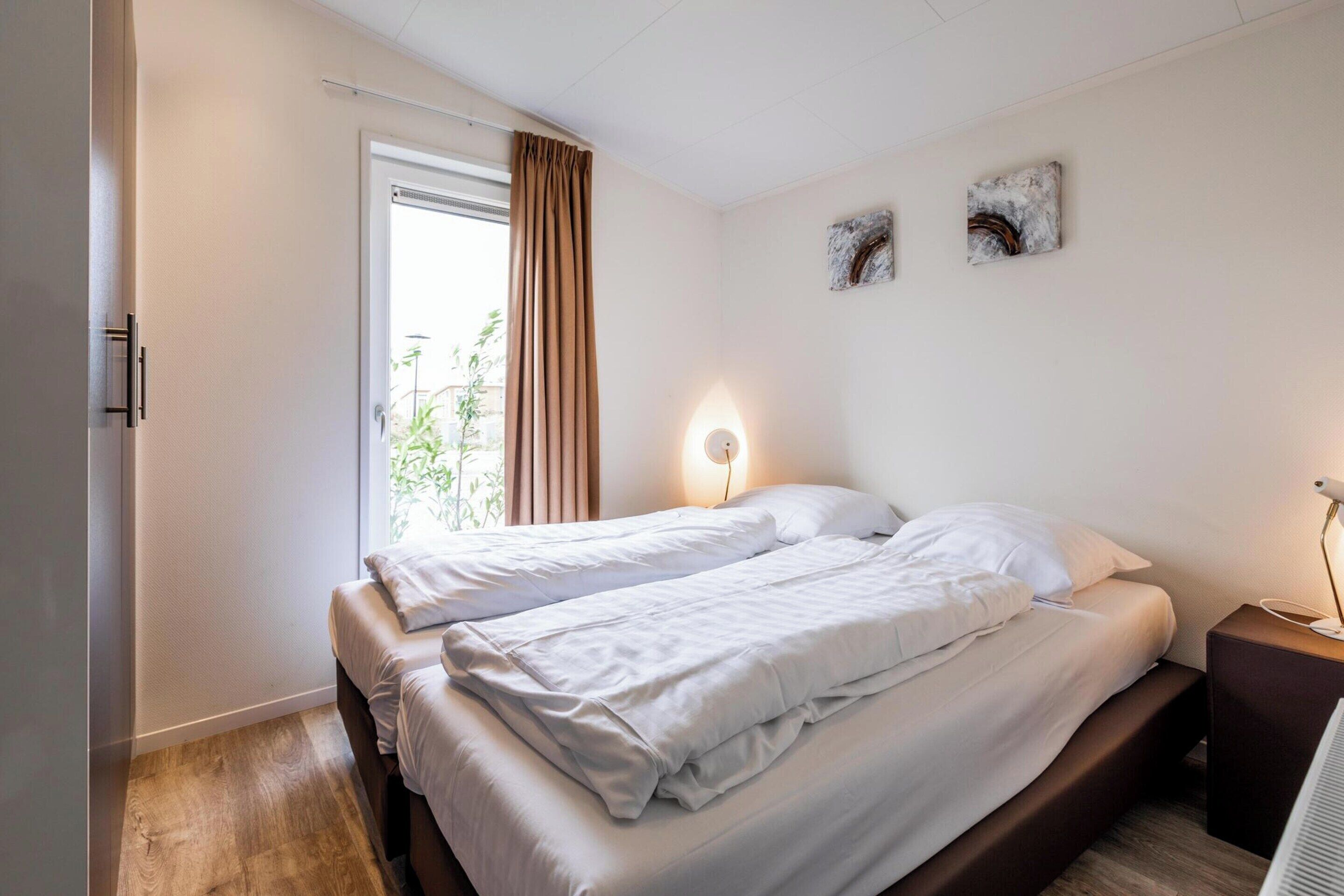 A bedroom with a bed, a bedside table, a lamp, and a window with curtains.