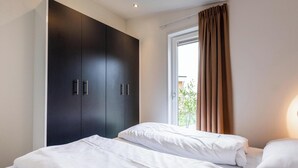 A hotel room with a large wardrobe, two beds, and a window with curtains. - Schaelsbergerbosch - Fireplace & Sauna (Bemelen)