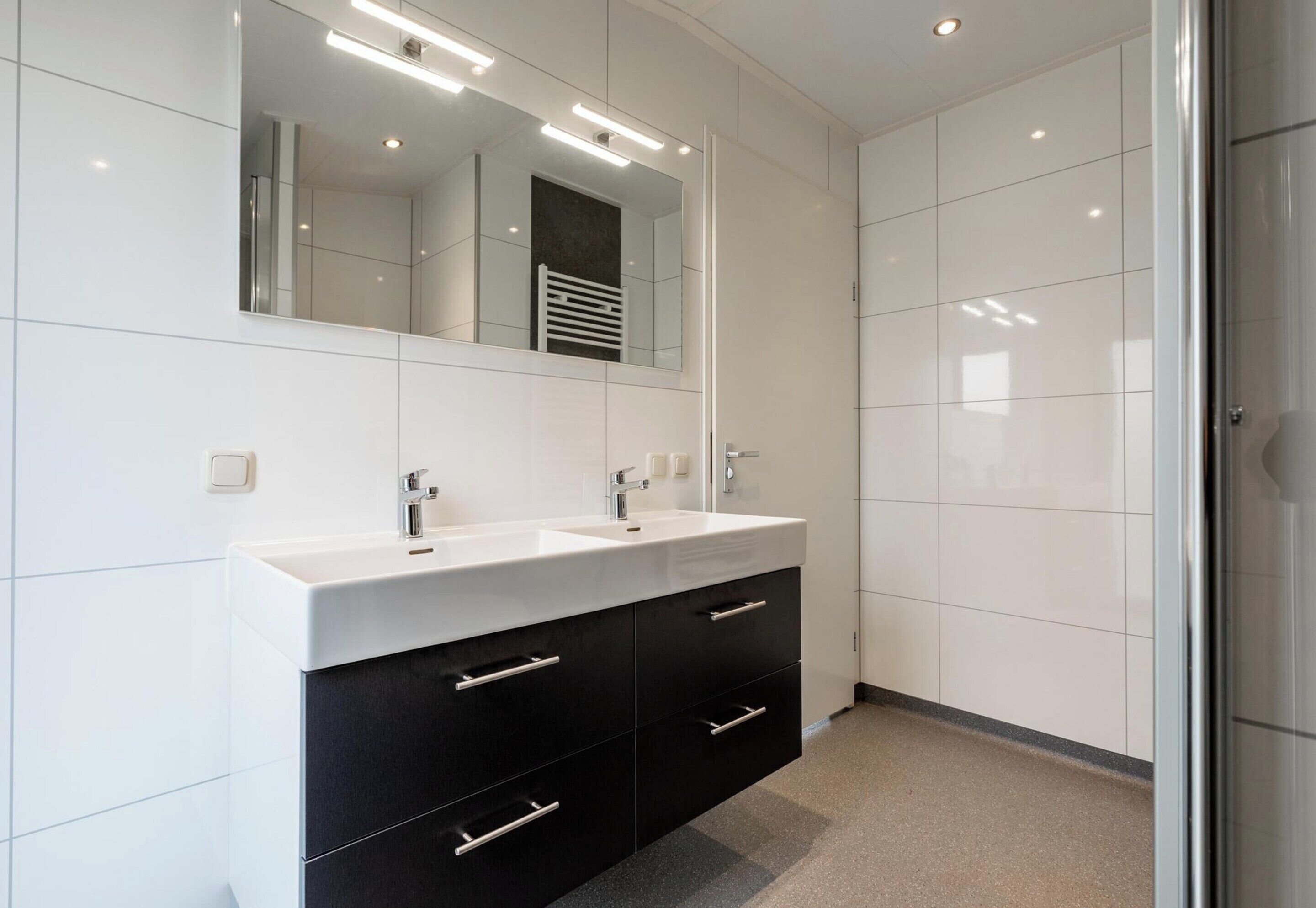 Une salle de bain moderne avec deux lavabos, un grand miroir et une douche à l’italienne.