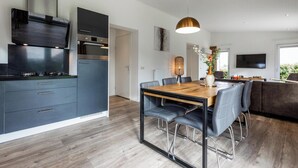 A modern kitchen with dark cabinetry, a built-in oven, and a dining area with a wooden table and chairs. - Schaelsbergerbosch - Fireplace & Sauna (Bemelen)
