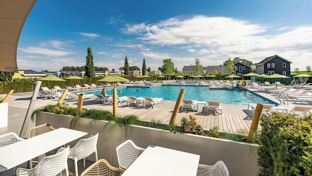 A poolside area with lounge chairs and tables, a swimming pool, and a view of surrounding buildings. - Schaelsbergerbosch - Fireplace & Sauna (Bemelen)